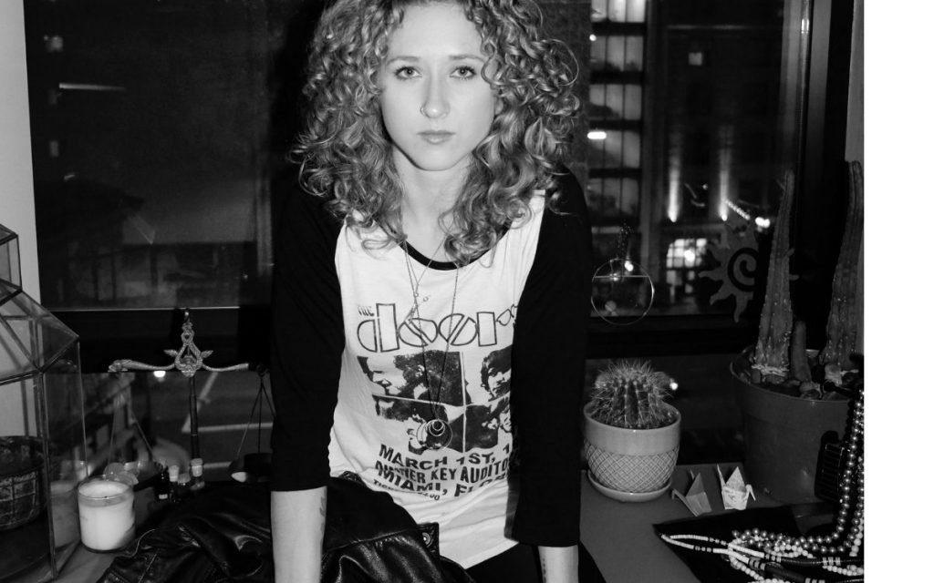 A women sits wearing a Doors t-shirt with a tour date on it.
